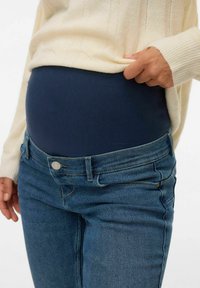 Trudničke traperice s tamnoplavim panelom iznad trbuha, srednje plava traper, dizajn s pet džepova i metalnim dugmetom sprijeda.