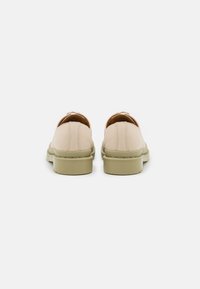 Beige slip-on boty s hladkým povrchem, zaoblenou špičkou a silnou, texturovanou olivově zelenou podrážkou. Žádné viditelné kovové prvky ani vzory.