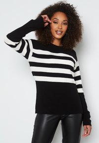 Maglione a strisce bianco e nero lavorato a maglia con maniche lunghe. Presenta una texture a coste e una vestibilità comoda, con strisce contrastanti nelle sezioni superiore e inferiore.