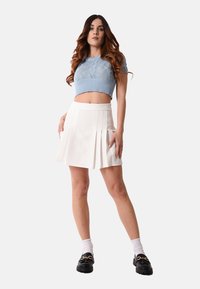 Maglione di lana azzurro chiaro a maniche corte con un motivo testurizzato, abbinato a una gonna bianca plissè e mocassini neri con dettagli in hardware dorato.