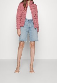 Růžová prošívaná bunda na zip z lehké tkaniny, kombinovaná s světle modrými džínovými šortkami s třepeným lemem. Celý vzhled doplňují průhledné sandály s pásky.