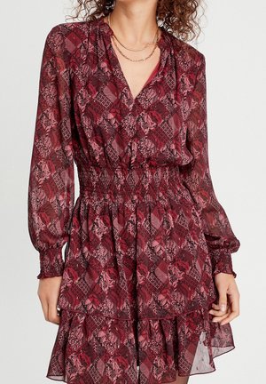 Robe à motif floral en bordeaux et rose. Confectionnée dans un tissu léger, elle présente un col croisé, une taille élastique et un ourlet à volants. Manches longues.