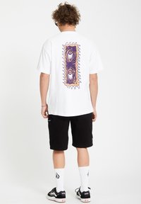 Hvid bomulds t-shirt med et lilla grafisk design på ryggen, parret med sorte shorts og hvide sokker med et logo.