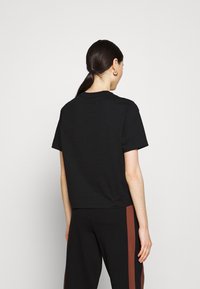 Černé zkrácené tričko s krátkým rukávem vyrobené z jemné bavlny, s kulatým výstřihem, které má minimalistický design bez viditelných log nebo vzorů.
