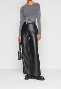 Grå ribbad långärmad crop top med logotyp vid fållen; högmidjade svarta läderbyxor med vida ben; svart handväska och kraftiga stövlar.