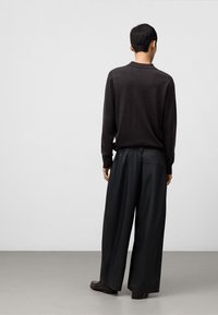 Mörkgrå långärmad tröja med avslappnad passform, tillsammans med vida svarta byxor med en bakficka, sedd bakifrån.