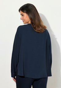 Blusa blu navy realizzata in tessuto morbido, con maniche lunghe e polsini con bottone, dal taglio morbido e con spacchi laterali all'orlo.