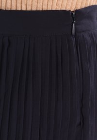 Gonna plissè di un blu navy scuro con una cintura liscia e una cerniera laterale. Il tessuto ha una texture leggera e fluida. Le pieghe verticali creano un aspetto strutturato.