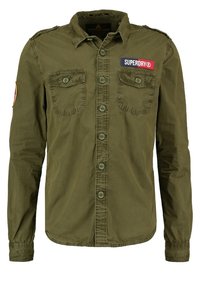 Maglietta a maniche lunghe verde oliva in cotone, con chiusura a bottoni frontale, due tasche sul petto e un evidente logo patch di Superdry.
