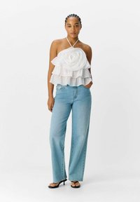 Witte gelaagde top met een bloemenontwerp, voorzien van een halternek. Gepaard met lichtblauwe wijde jeans en zwarte sandalen.