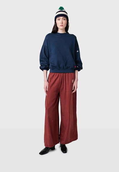Marinblå bomullströja med lös passform, kombinerad med röda vida byxor med en broderad patch, kompletterad med en randig mössa.
