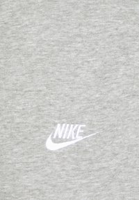 Sivá mikina vyrobená z jemného, textúrovaného materiálu, s malým bielym logom Nike na hrudi. Jednoduchý, pohodlný dizajn.