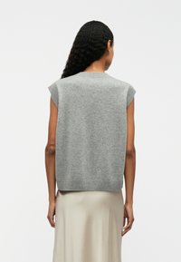 Gilet gris sans manches avec un col et un ourlet côtelés, fabriqué en matériau doux, présentant une texture lisse et une coupe décontractée.