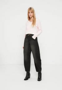 Camisola de malha cor de rosa claro com mangas compridas, combinada com jeans pretos de cintura alta e corte largo e botins pretos de salto.