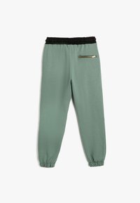 Helle grüne Jogginghosen aus weichem Material, mit einem schwarzen elastischen Bund, Bündchen an den Knöcheln und einer Reißverschlusstasche.