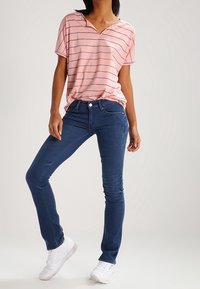 Růžový pruhovaný top s krátkým rukávem a výstřihem do V, kombinovaný s tmavě modrými skinny džíny a bílými teniskami. Neformální outfit s volným střihem.