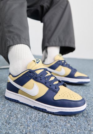 Baskets Nike bleues et jaunes avec des accents blancs, présentant une tige en cuir lisse, un bout perforé et une semelle en caoutchouc contrastée.