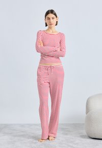 Μπλούζα με μακριά μανίκια σε κόκκινο και άσπρο ριγέ, και παντελόνι πιτζάμας που ταιριάζει, με ελαστική μέση και κορδόνι, κατασκευασμένα από απαλό ύφασμα.