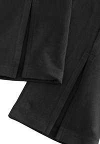 Top de tela negra con mangas cortas, que presenta aberturas laterales y una textura suave. Las costuras están cuidadosamente cosidas para mayor durabilidad.