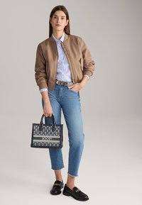 Bruine bomberjack, lichtblauw gestreept overhemd, blauwe jeans, zwarte loafers, zwarte handtas met bloemenpatroon en JOOP! merk.