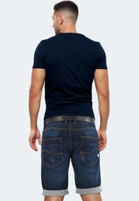 Marineblaues T-Shirt kombiniert mit dunklen Denim-Shorts mit umgeschlagenen Säumen, einer glatten Struktur, kontrastierenden Nähten und Gesäßtaschen mit einem dezenten Design.