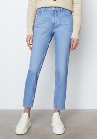 Světle modré džíny s rovnými nohavicemi, vysokým pasem a viditelným švem. Vybavené bílými teniskami s akcentem limetkově zelené barvy.