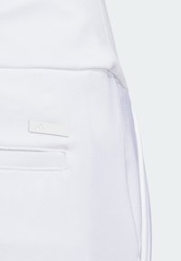 Vita träningsbyxor med en platt ficka och en liten rektangulär etikett med präglad logotyp. Mjuk, slät tygtextur.