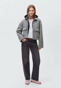 Veste en laine grise clair courte avec deux poches avant, assortie à un jean foncé avec des clous sur les côtés et des baskets roses. T-shirt blanc en dessous.