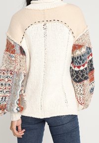 Svrchní svetr z hrubého pletení s krémovým tělem, pastelovým panelem na ramenou a barevnými vzorovanými rukávy s texturovanými detaily. Žebrované manžety.