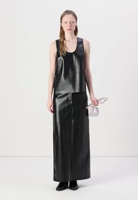 Black leather sleeveless top and long skirt, featuring a smooth texture. Model holds a small light-colored bag. Classic, minimal design.