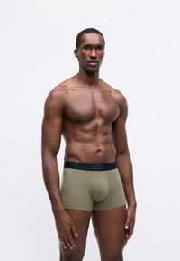 Boxer shorts de algodón verde con una cinturilla elástica negra que presenta el logo "HUGO", diseño ajustado, textura suave y corte de longitud media.