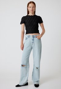 Sort cropped top med tekstureret mønster, lyseblå baggy jeans med slidte knæ, og sorte spidse flade sko. Simpel og moderne design.