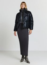 Giacca a vento nera con finitura lucida, colletto alto e chiusura con zip, abbinata a un dolcevita grigio aderente e a una gonna grigia liscia.