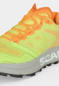 Chaussure de sport jaune vif et orange avec lacets, semelle grise, et texte "AXIAL TR/TECH" et "SCARPA" sur le côté.