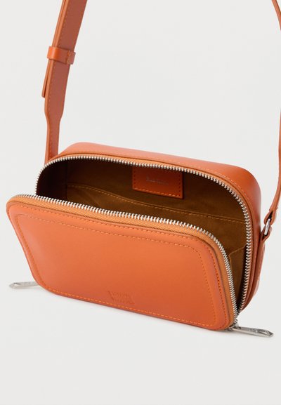 Μικρό ταν δερμάτινο τσαντάκι ώμου με δύο ασημένια φερμουάρ μερικώς ανοιχτά, που δείχνουν εσωτερικό από καφέ ύφασμα και ρυθμιζόμενο λουράκι.