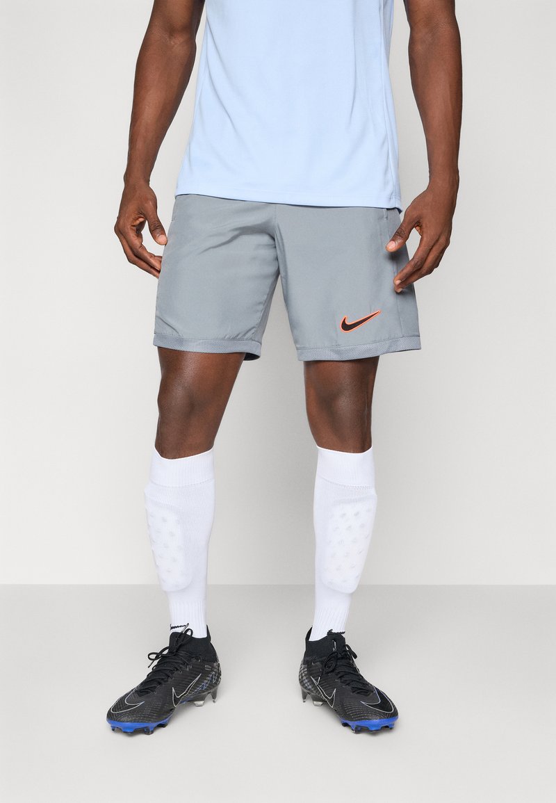 Shorts Nike gris, logo orange, associés à des chaussettes blanches montantes et des crampons noirs avec des accents bleus. Ajustement proche, matériau l�éger.