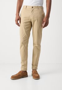 Beige katoenen broeken met een rechte pasvorm, voorzien van een knoopsluiting en zijzakken, gecombineerd met bruine suède instapschoenen.