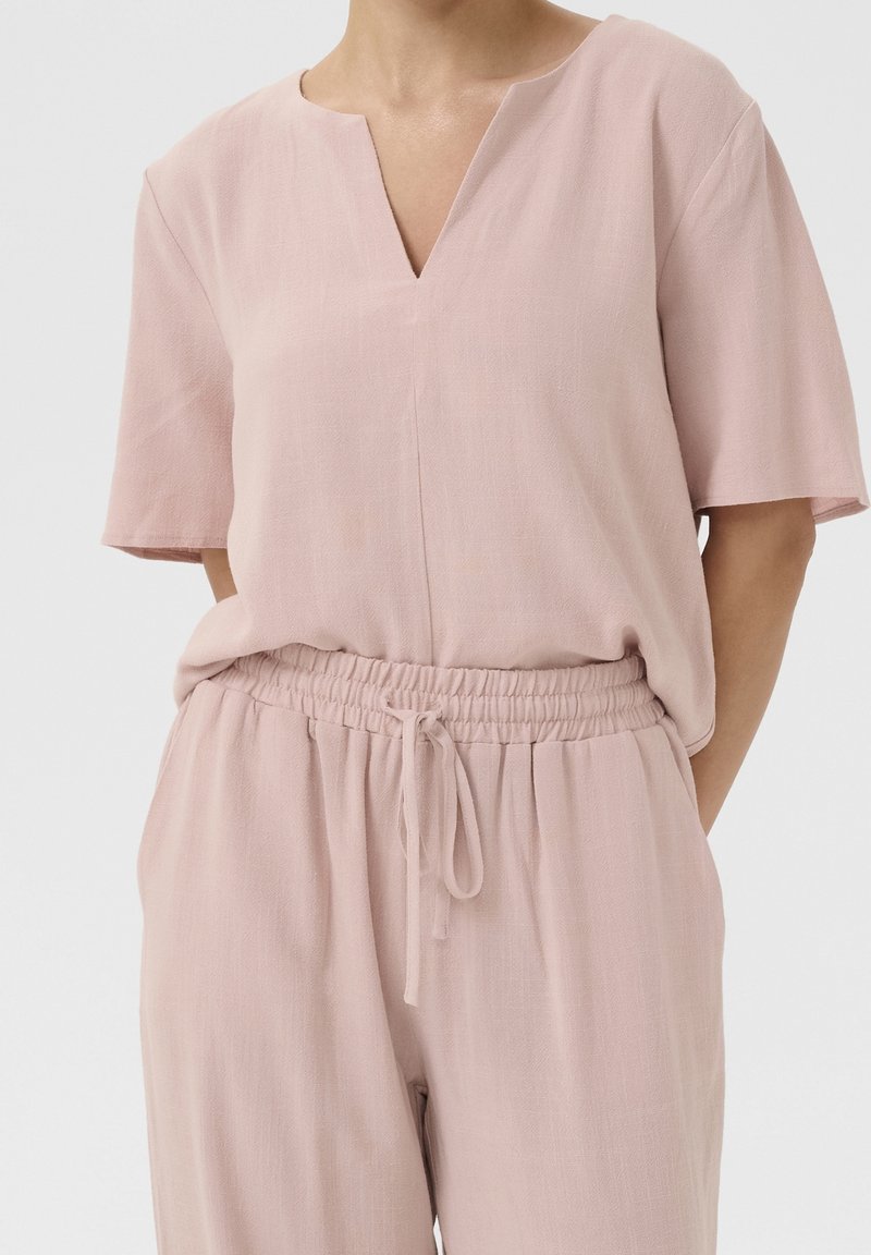 Top rosa chiaro a maniche corte con scollatura a V, realizzato in un tessuto texturizzato; abbinato a pantaloni coordinati con vita elastica.