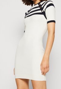 Robe à manches courtes côtelée en blanc avec rayures bleu marine. Caractérisée par des accents de boutons et une silhouette ajustée. Texture lisse, coupe au genou.