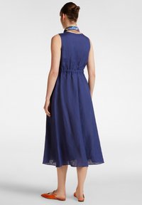 Abito senza maniche in lino blu navy con vita cintrata, orlo fino al ginocchio e silhouette leggermente svasata. Abbinato a scarpe flat arancioni.