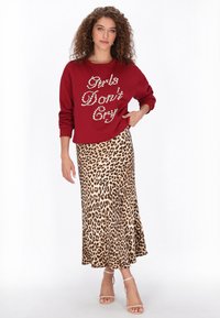 Vörös pulóver fémes betűkkel, hozzáillő leopárdmintás midi szoknya, amelyen bővülő szegély és pántos, áttetsző szandálok találhatók.