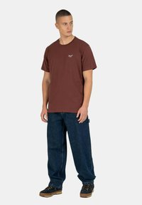 Camiseta de algodón marrón con mangas cortas y cuello redondo, combinada con vaqueros de denim azul holgados y zapatos oscuros con cordones.