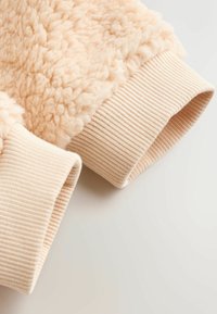 Fleece sweatshirt sleeve in soft peach color, featuring textured fabric and ribbed peach cuffs. Smooth, fluffy texture with a cozy appearance.