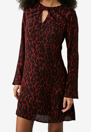 Kobieta ubrana w czerwoną i czarną sukienkę z długim rękawem, wzorem w lamparta oraz małym otworem przy dekolcie.