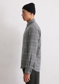 Grijs geblokt overhemd met een button-down kraag, lange mouwen en afgeronde zoom. Draag het met een zwarte beanie, die een textielstructuur laat zien.