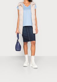 Gilet imbottito beige, maglietta azzurra a V, gonna a tubino in denim scuro, stivaletti bianchi alla caviglia, con una borsa a tracolla blu navy. Elementi di design semplici e moderni.
