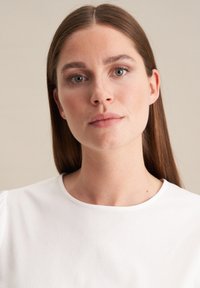 Top bianco a girocollo con maniche a palloncino corte, texture liscia, design minimale e senza motivi o dettagli hardware visibili.