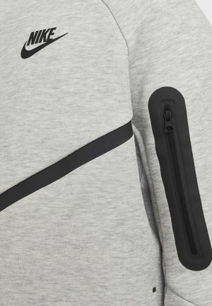 Felpa grigia Nike con logo nero, accenti neri e una tasca con zip sulla manica, realizzata in un tessuto morbido e testurizzato.