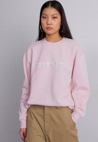 Felpa rosa chiaro con collo rotondo, caratterizzata da un logo "carhartt" ricamato bianco. Realizzata in morbido tessuto, con maniche lunghe e polsini a coste.