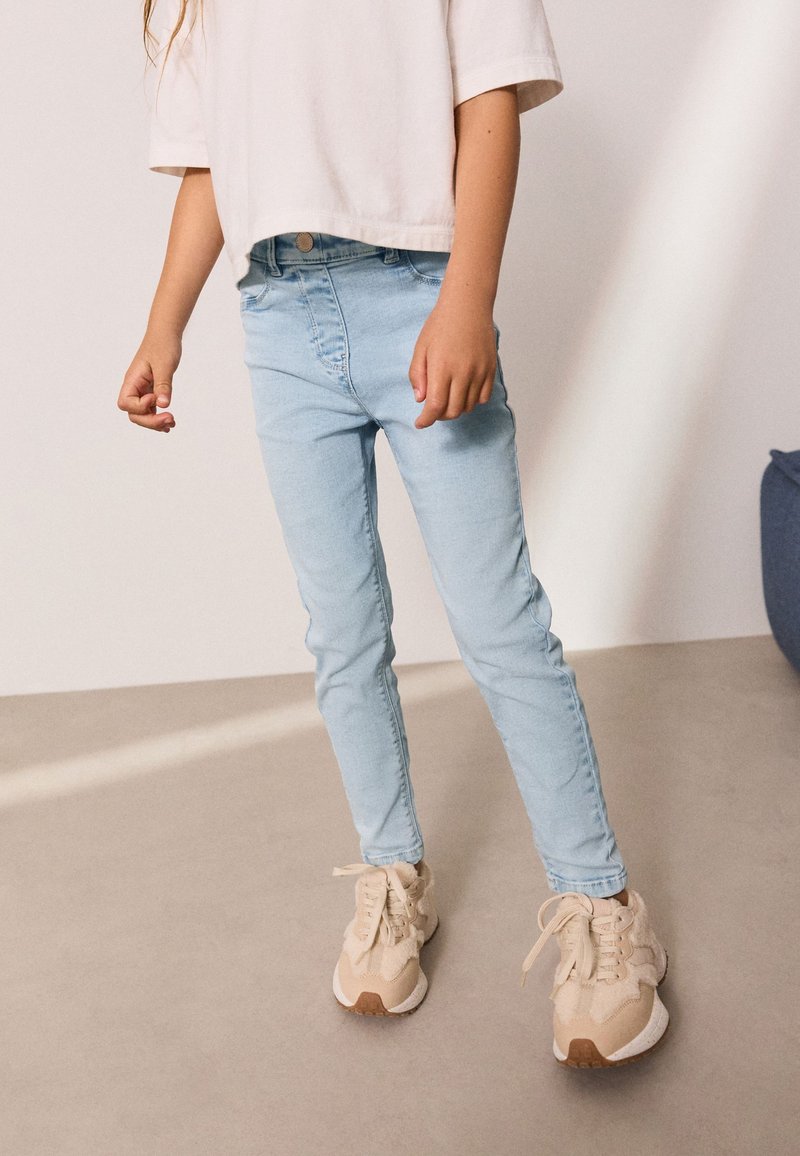 Lysblå skinny jeans lavet af denim, kombineret med beige sneakers med en struktureret overflade og snørebånd. Enkel kort hvid t-shirt.